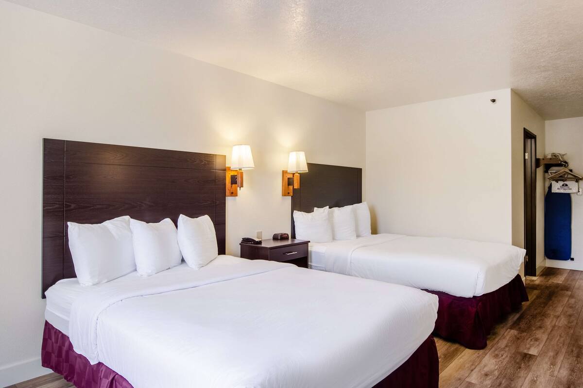 A hotel room with two beds, a wooden headboard, bedside lamps, a nightstand, and a wardrobe.
