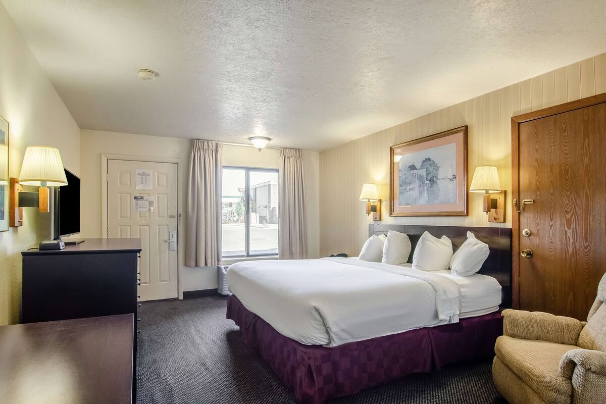 A hotel room with a large bed, a desk, a chair, and a television.