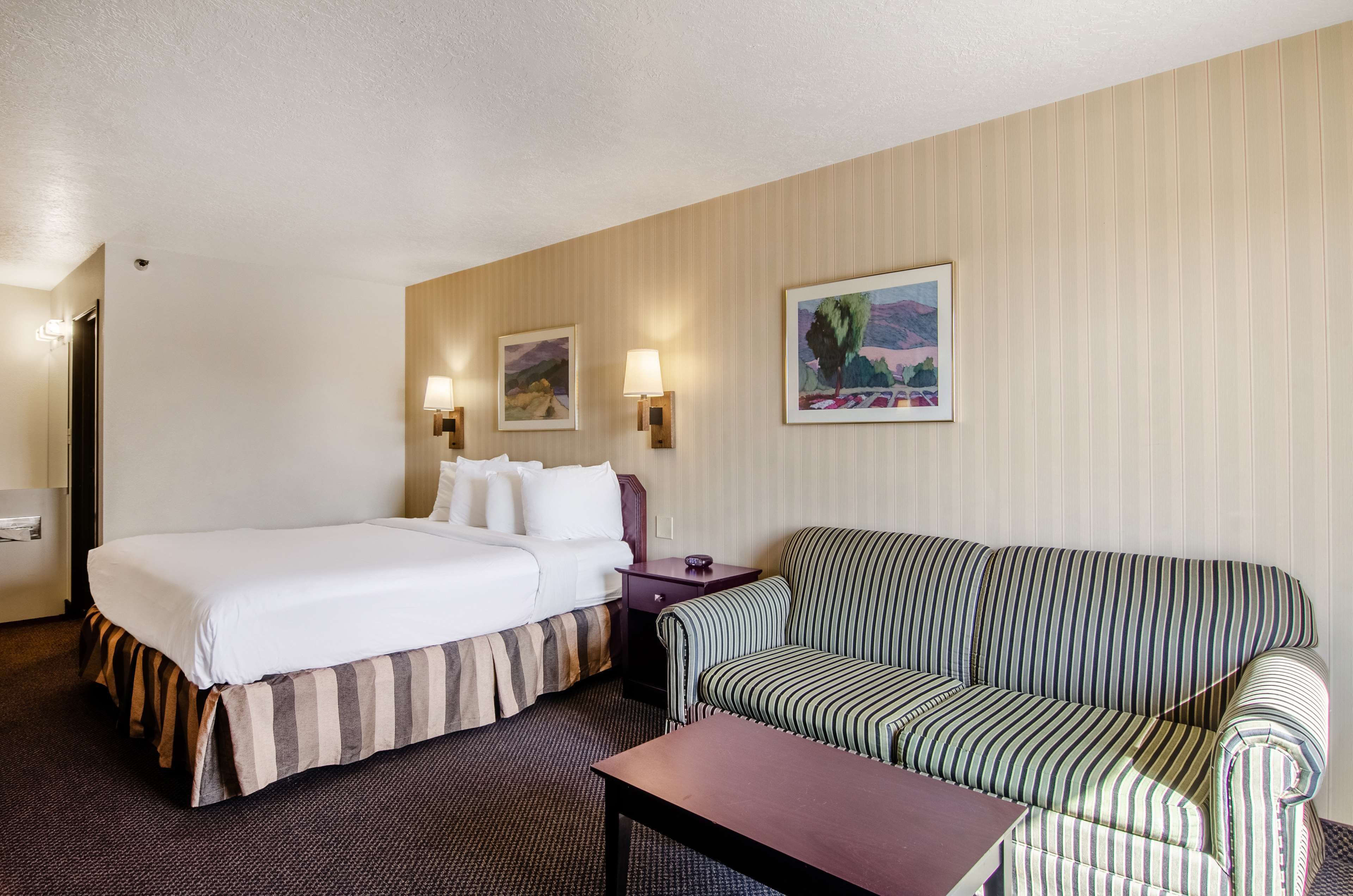 A hotel room with a bed, a striped sofa, a small table, and two wall-mounted lamps.