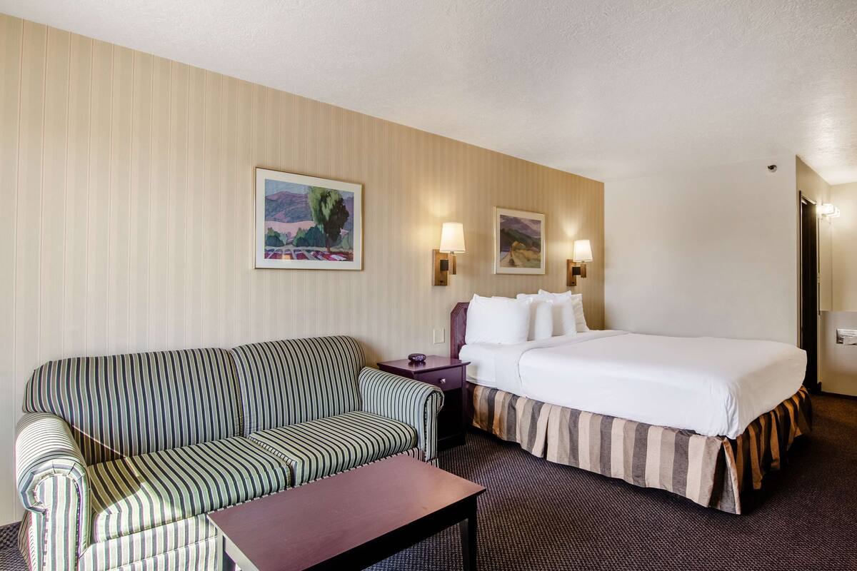 A hotel room with a striped sofa, a bed with a striped bedspread, a small table, and two wall-mounted lamps.