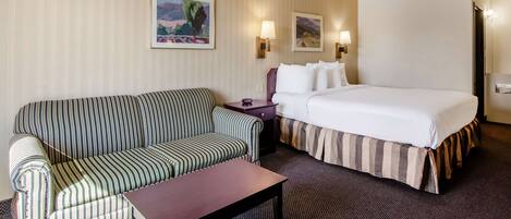 Ein Hotelzimmer mit gestreifter Couch, einem Bett mit gestreifter Bettdecke, einem kleinen Tisch und zwei Wandleuchten.