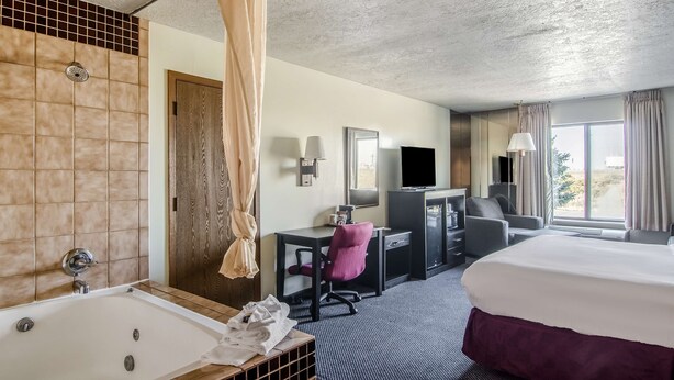 A hotel room with a large bed, a desk with a chair, a television, and a bathroom with a bathtub and shower. - Americas Best Value Inn & Suites Ft. Collins E at I-25 (Fort Collins)