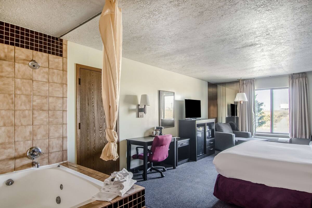 A hotel room with a large bed, a desk with a chair, a television, and a bathroom with a bathtub and shower.