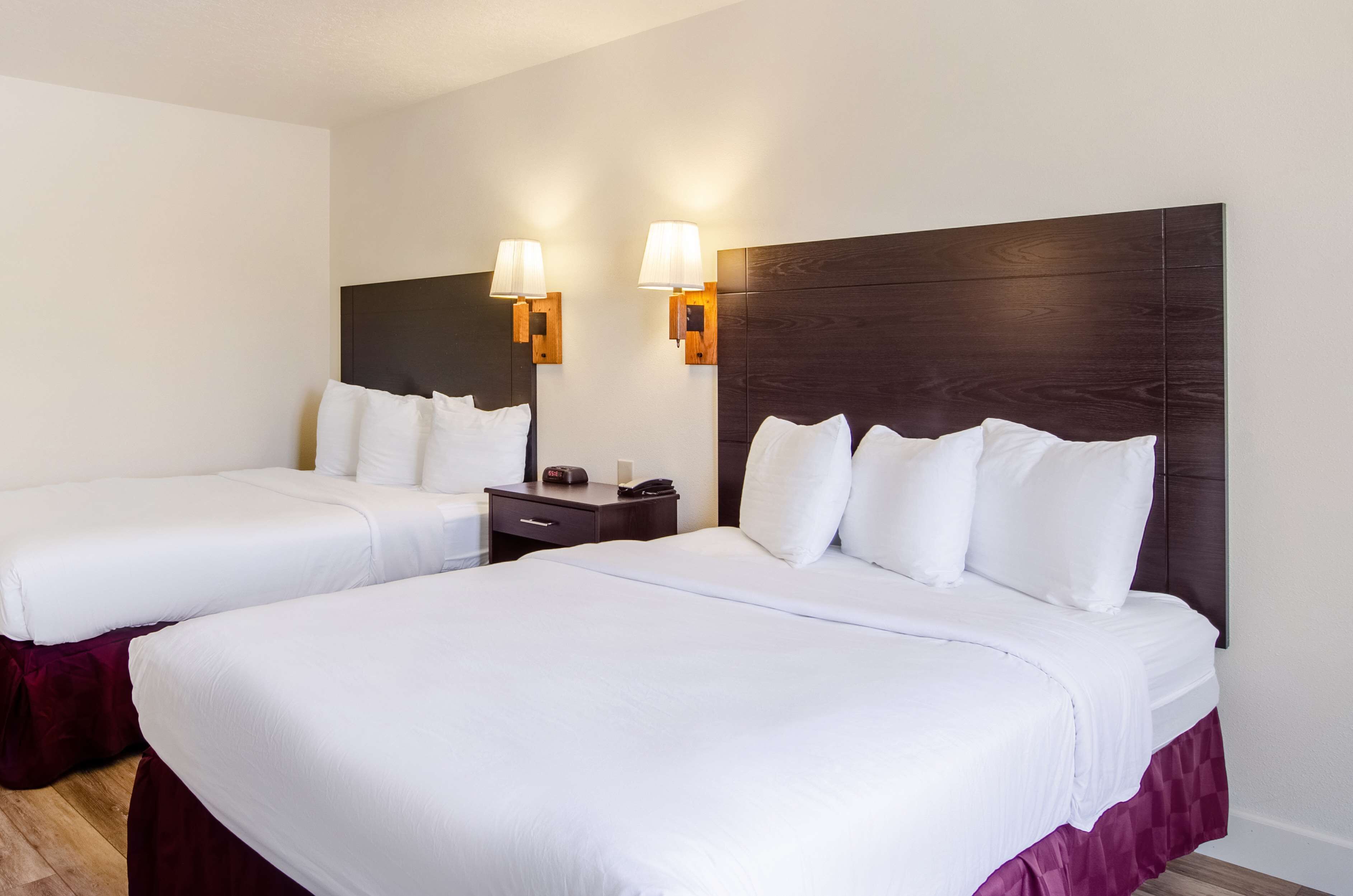 Une chambre d’hôtel avec deux lits, une table de chevet avec une lampe et une tête de lit en bois.