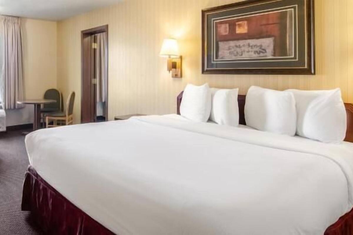 A hotel room with a large bed, a desk, a chair, and a wall-mounted lamp.