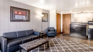 A modern living room with a sofa, armchair, and coffee table, a kitchen with a microwave and refrigerator, and a framed artwork on the wall. - Americas Best Value Inn & Suites Ft. Collins E at I-25 (Fort Collins)
