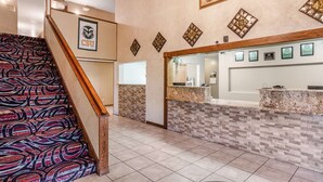 A reception area with a patterned carpeted staircase, a reception desk with a marble top, and a wall with framed certificates. - Americas Best Value Inn & Suites Ft. Collins E at I-25 (Fort Collins)