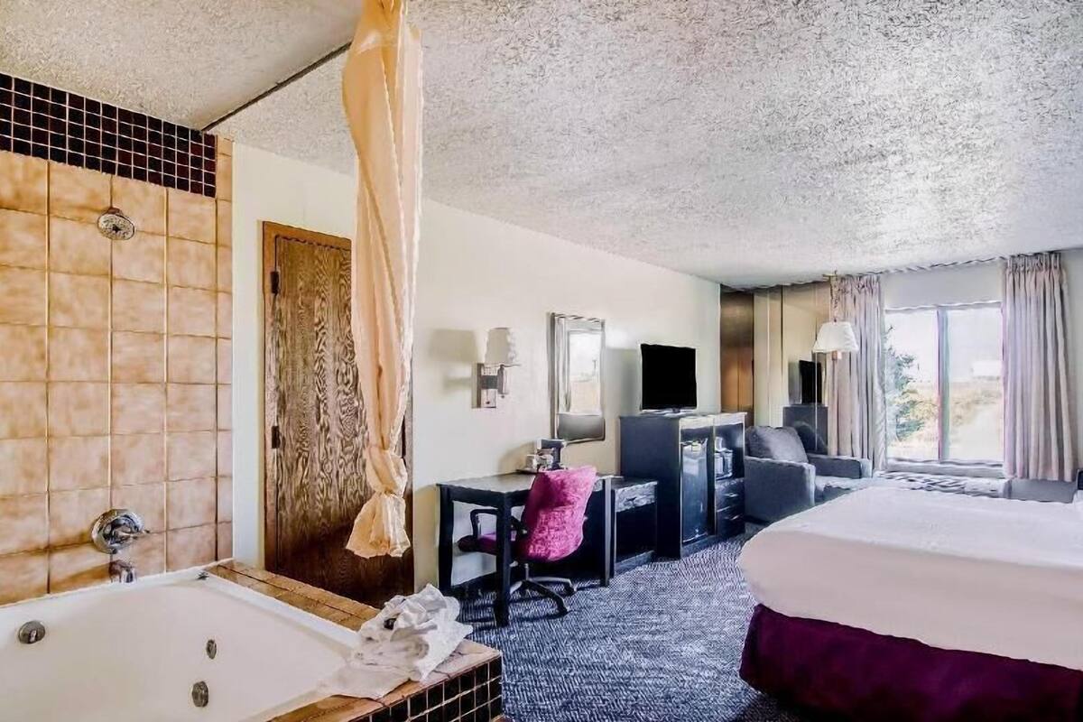 A hotel room with a large bed, a desk with a chair, a television, and a bathroom with a bathtub.