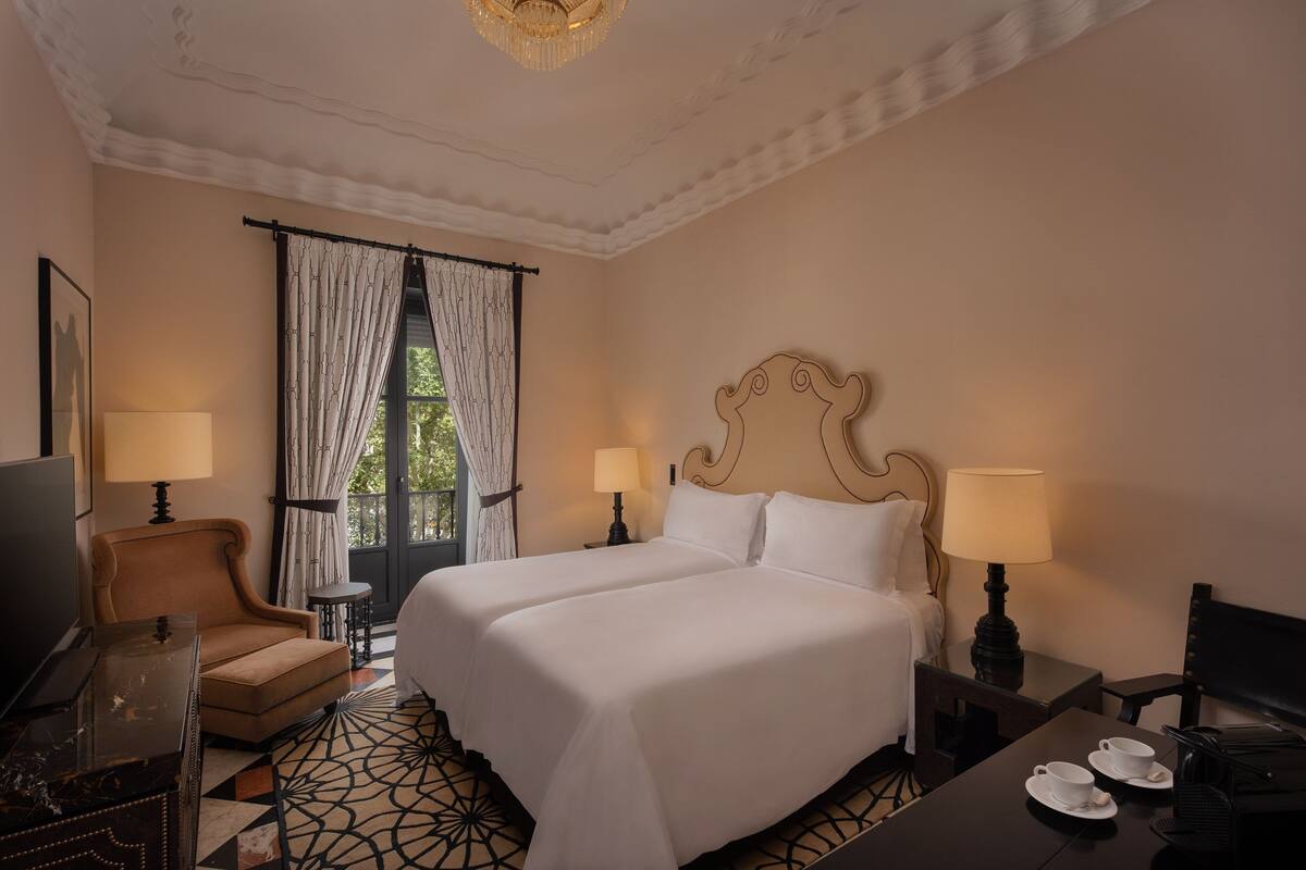 A hotel room with a large bed, two bedside tables with lamps, a chair, a desk with a computer, and a television.