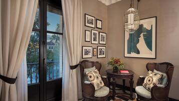 A room with two upholstered chairs, a round table with a vase of flowers, and a large framed artwork on the wall.