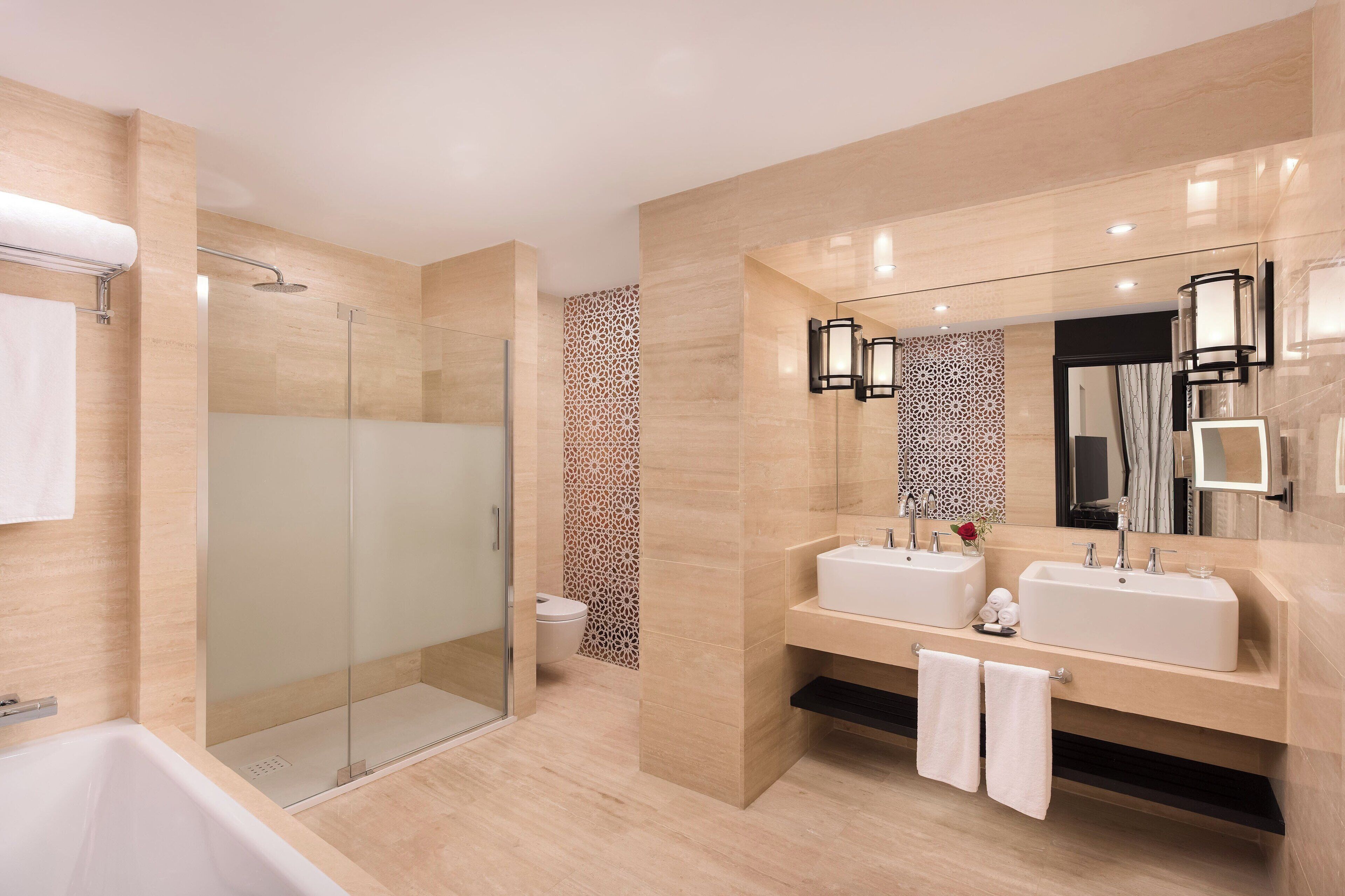 A modern bathroom with a glass-enclosed shower, two sinks, and a large mirror with wall sconces.