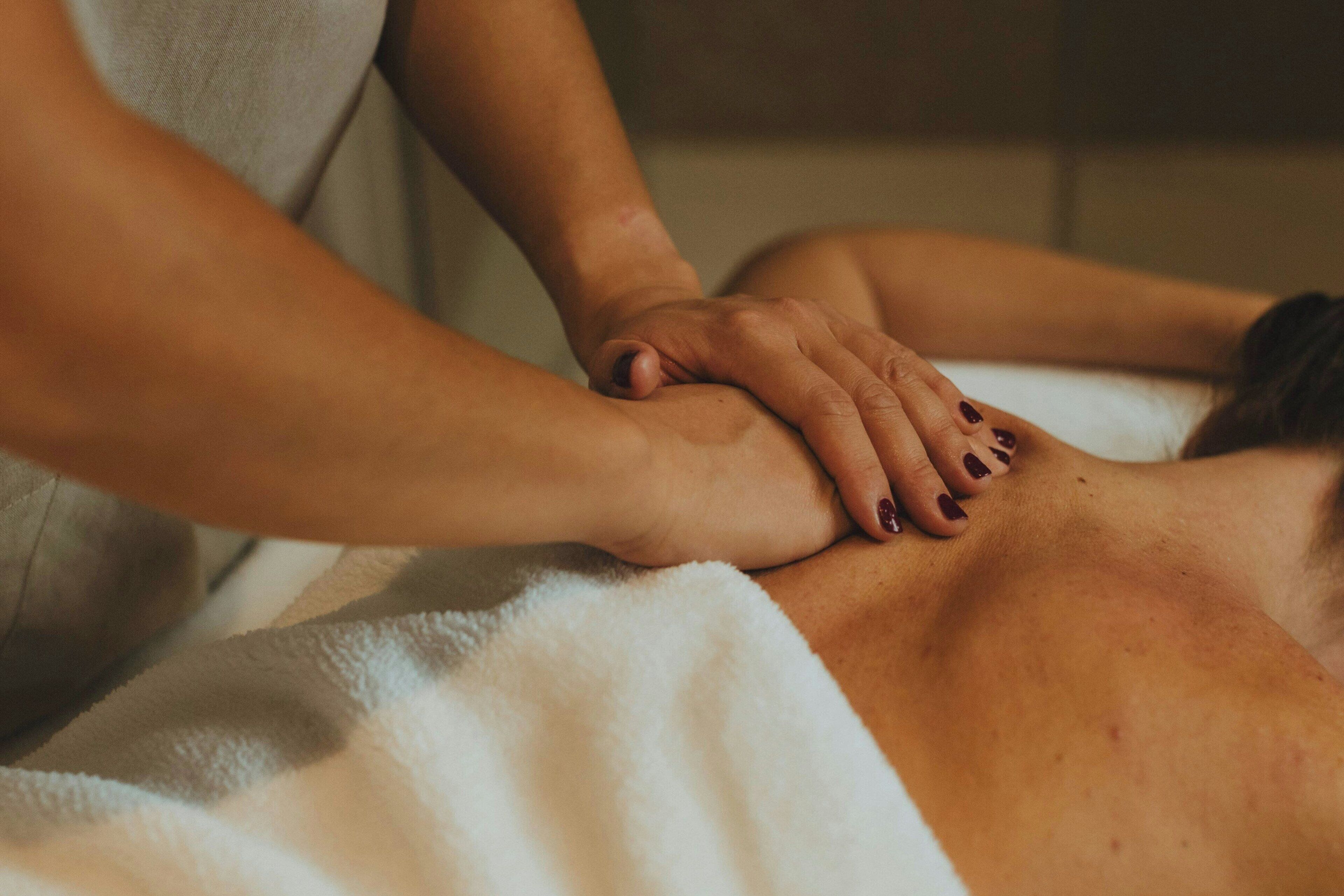 Une personne reçoit un massage, les mains du masseur étant posées sur son dos.