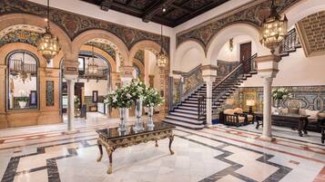 A grand lobby with ornate arches, a marble floor, and a staircase.