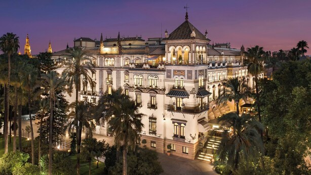 A large, ornate building with multiple balconies and a central dome, surrounded by palm trees.