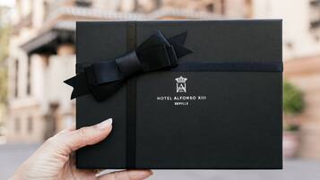 Una caja de regalo negra con un lazo y cinta negros, etiquetada como "HOTEL ALFONSO XIII SEVILLE".