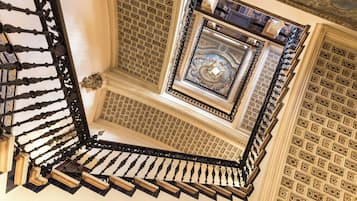 Una imponente escalera con barandales de metal ornamentados y un techo decorativo.