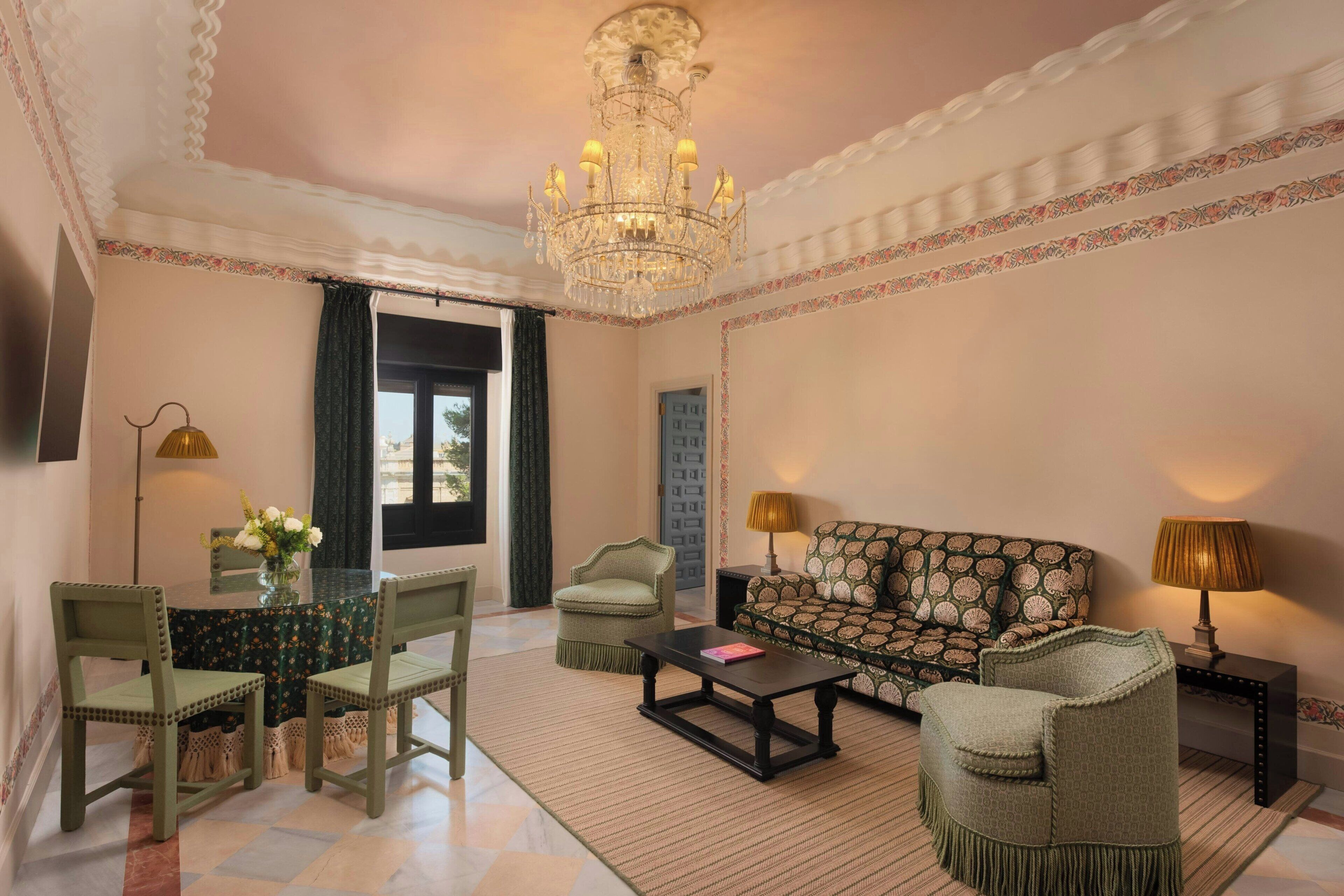 A spacious living room with a chandelier, a sofa, a coffee table, and a dining area with chairs and a table.
