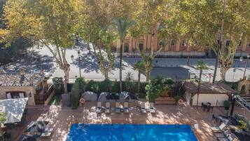 Una piscina en la azotea con sillas de descanso y sombrillas, rodeada de árboles y edificios.