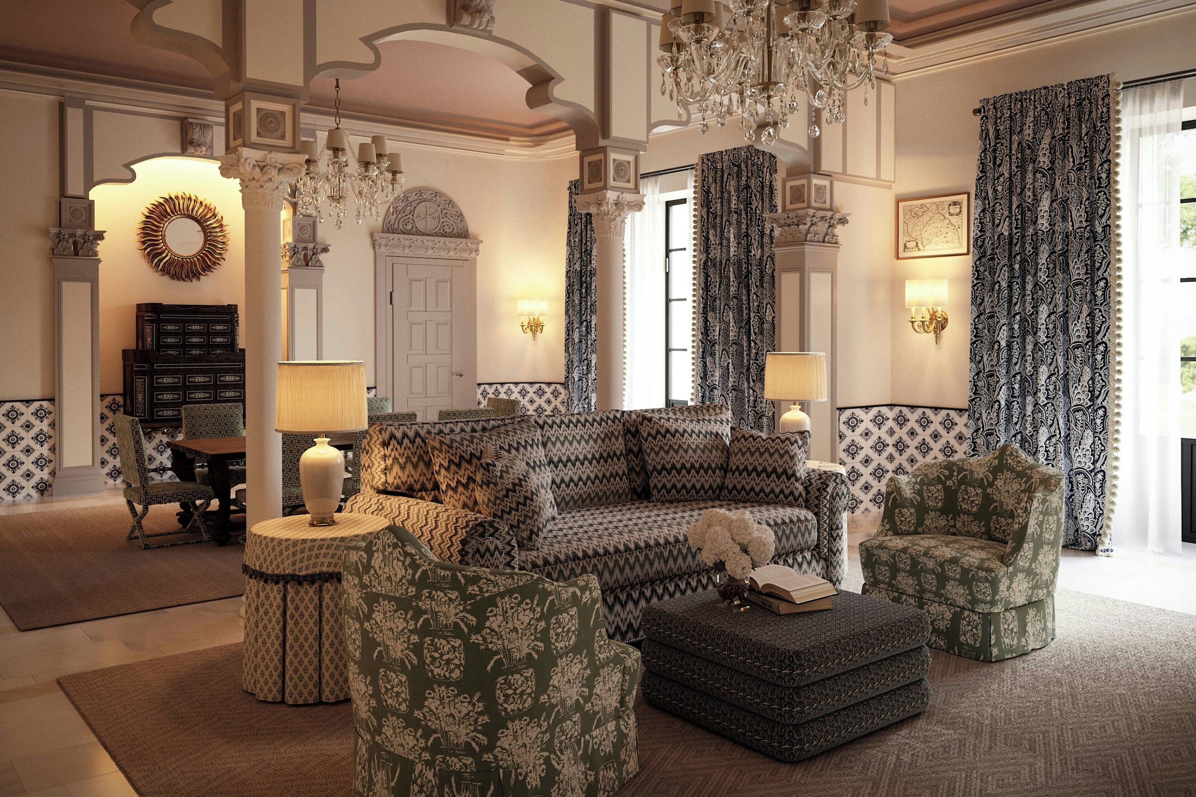 A spacious living room with a large sectional sofa, patterned armchairs, and ottomans. There are decorative lamps, a chandelier, and a fireplace with a mantel.
