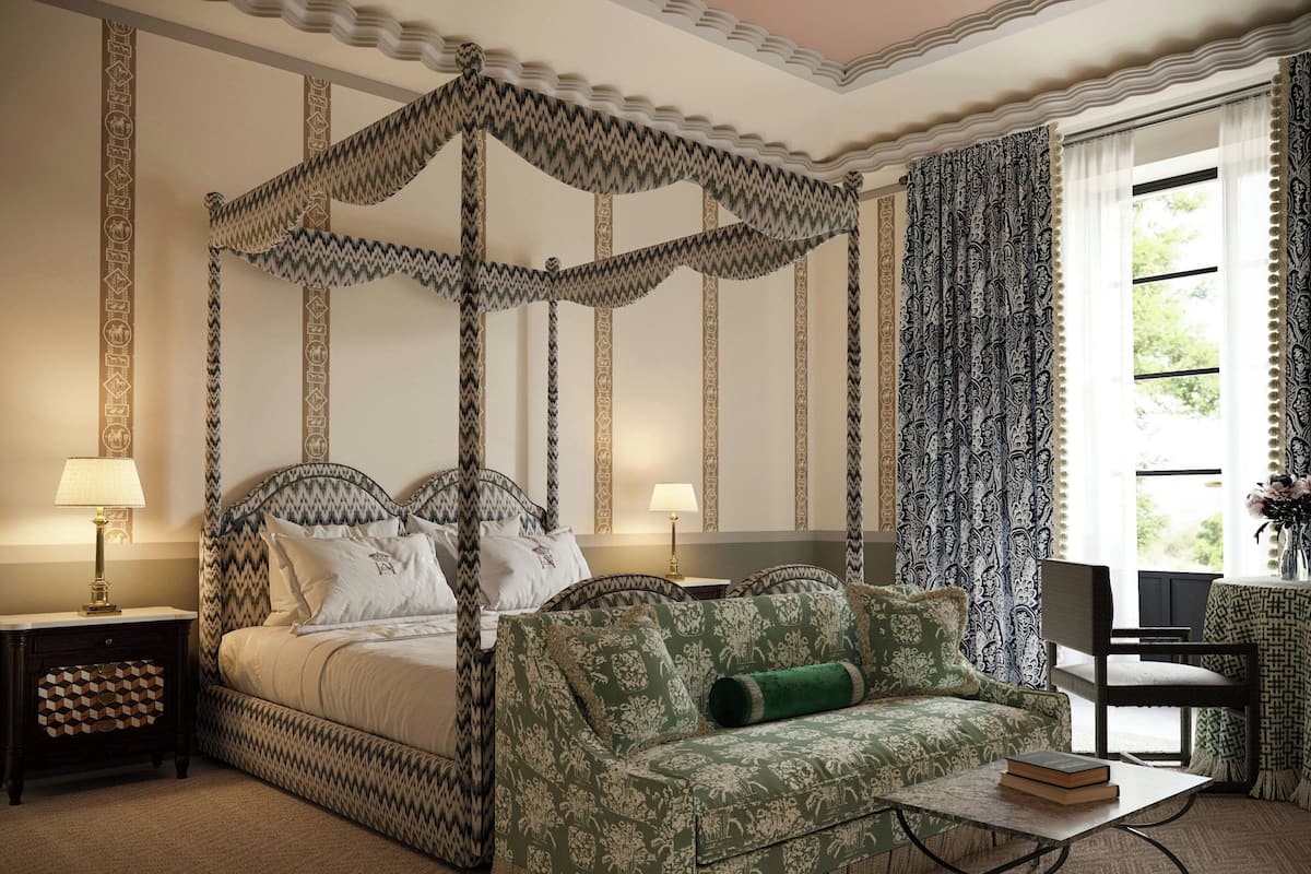 A four-poster canopy bed with a green upholstered sofa and a small table with a book.