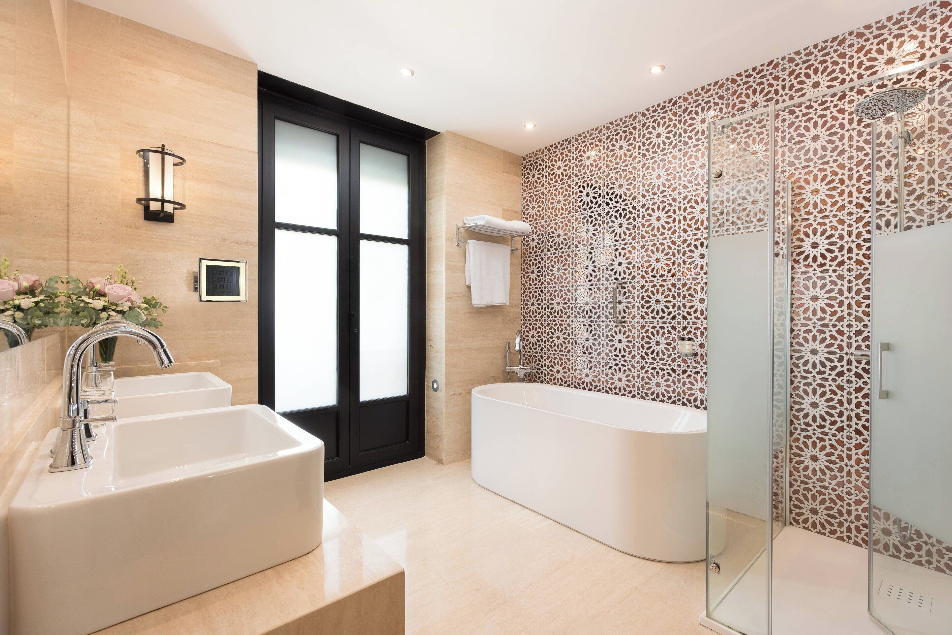 A modern bathroom with a large bathtub, two sinks, and a glass-enclosed shower.