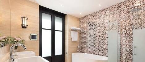 A modern bathroom with a large bathtub, two sinks, and a glass-enclosed shower.