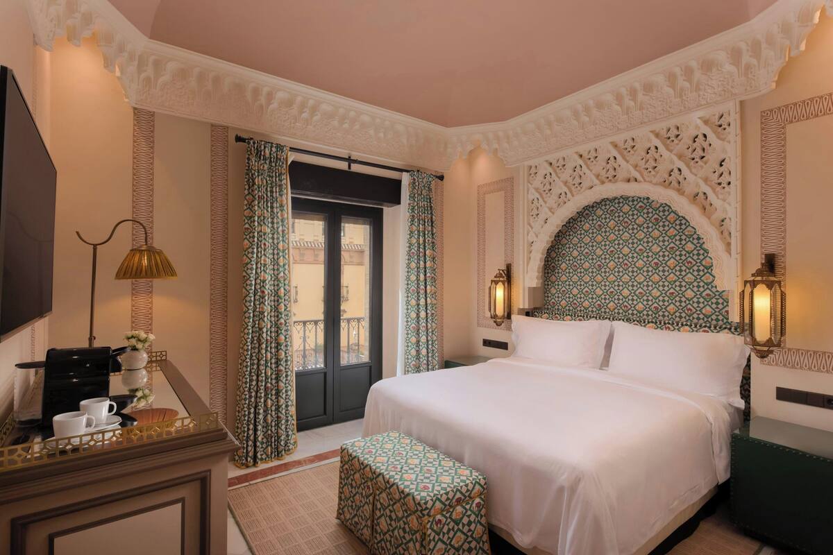 A hotel room with a large bed, a desk with a coffee maker, and patterned curtains.