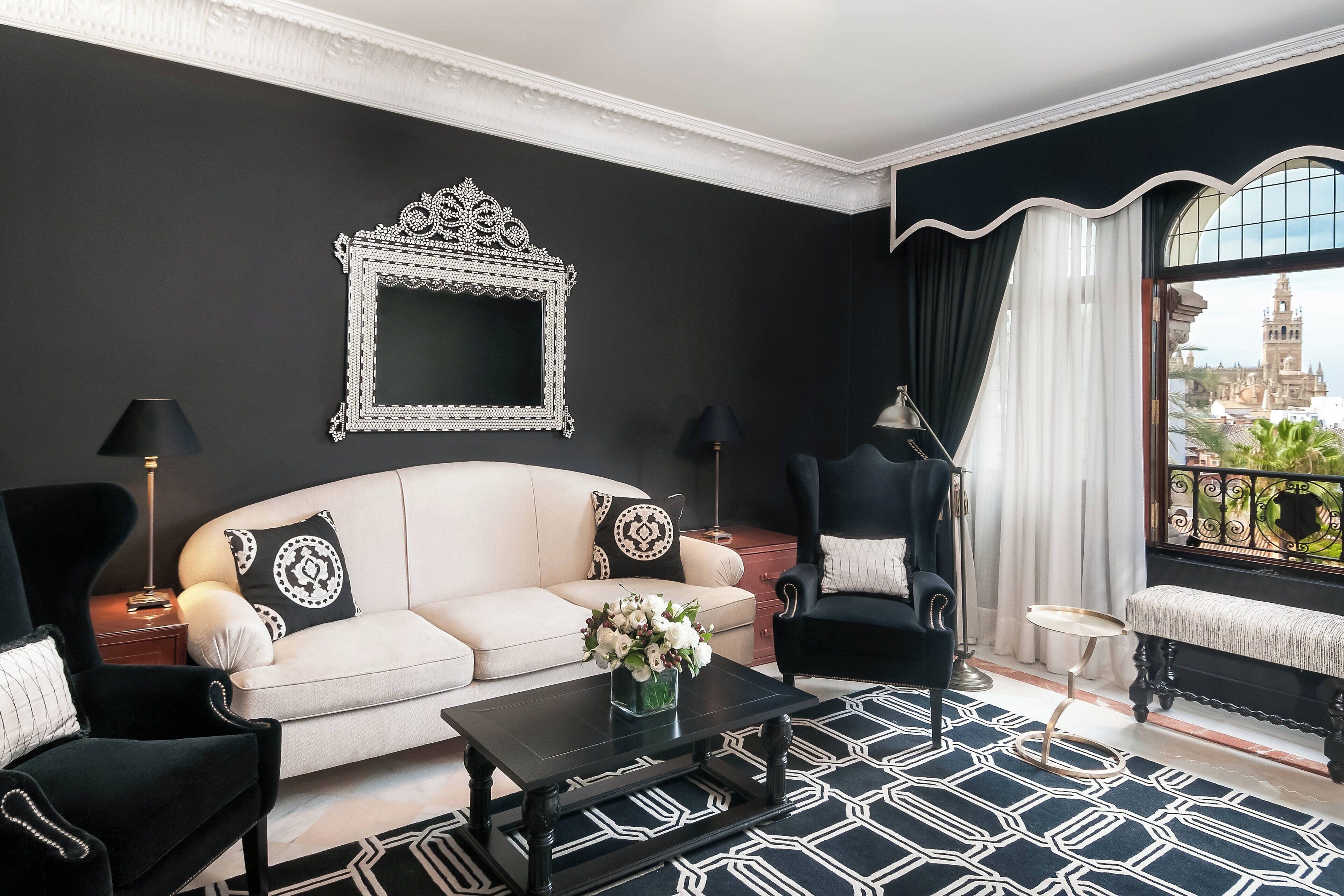 Un salón con un sofá blanco, sillones negros, una mesa de centro negra y un espejo decorativo en la pared.