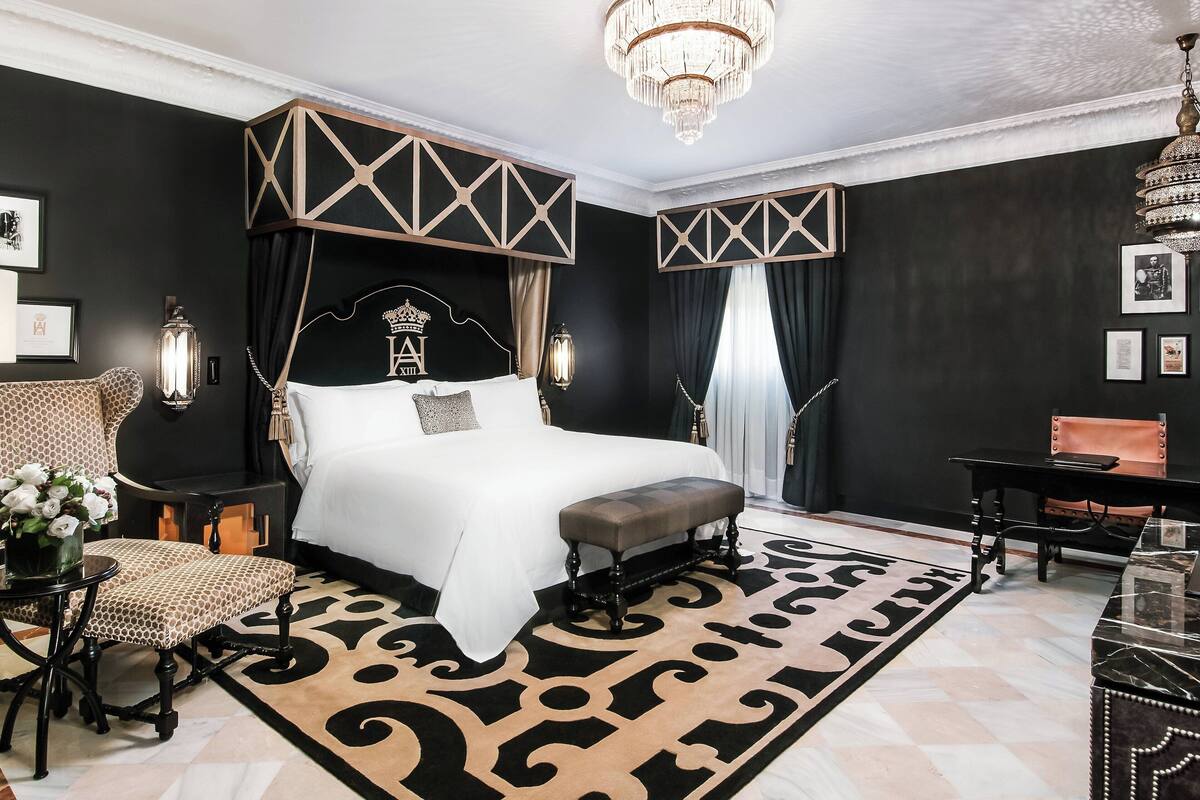 A spacious bedroom with a large bed, a bench, a desk, and a chandelier.
