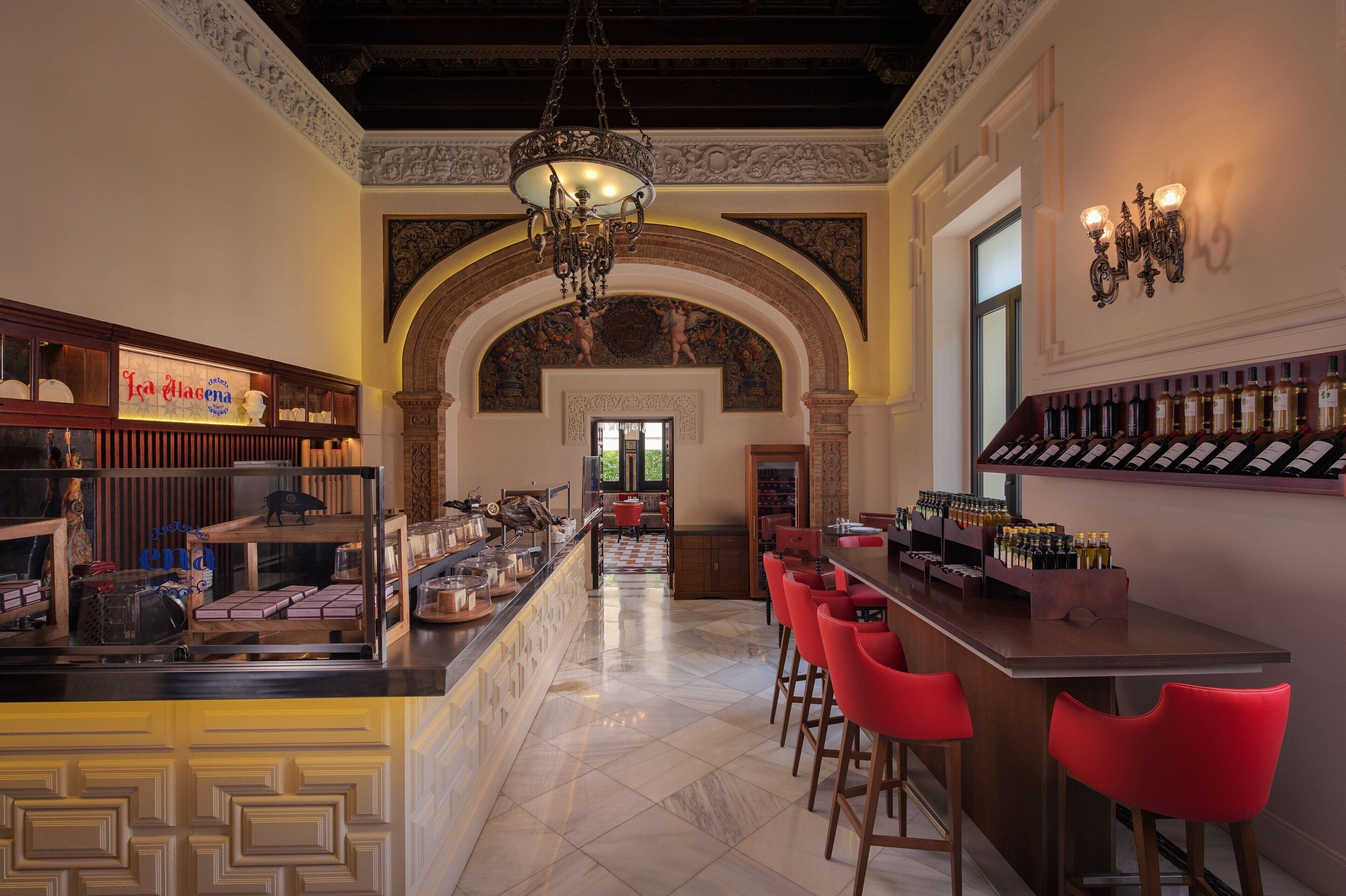 Una zona de bar con una barra larga, taburetes rojos y una exhibición de vinos.