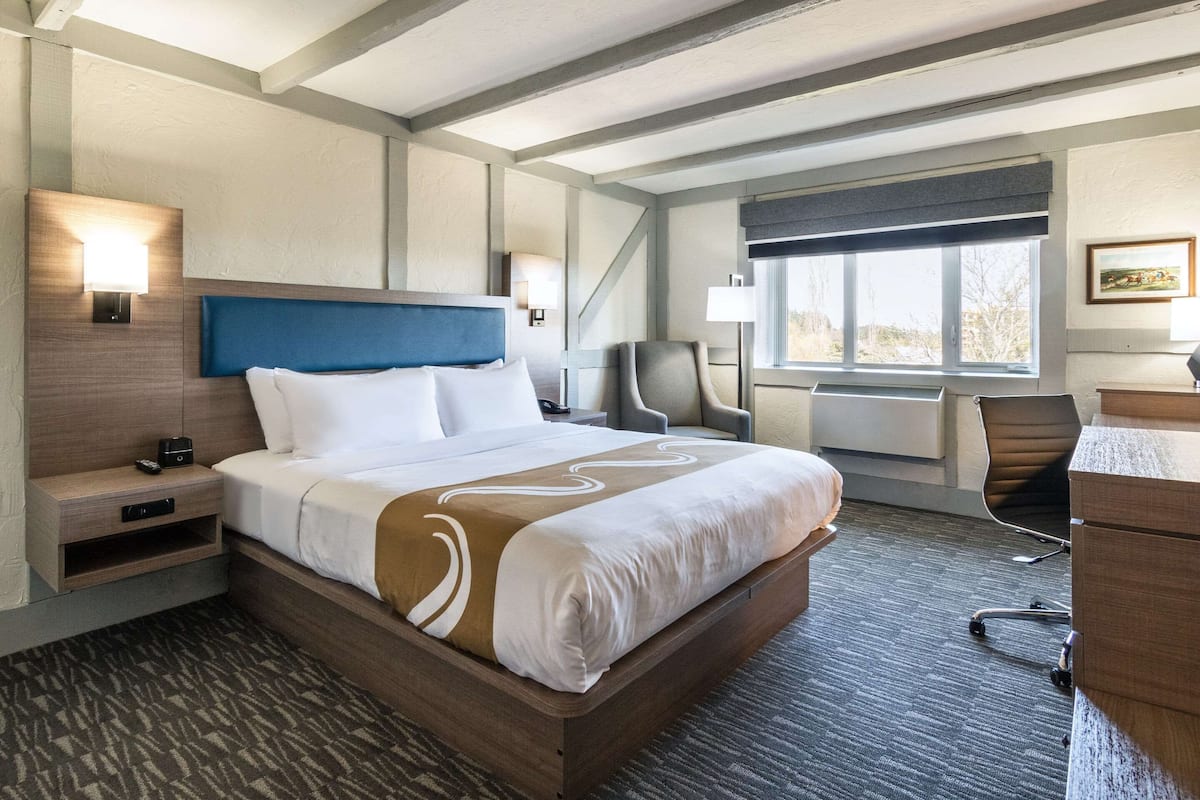 A hotel room with a large bed, a desk, a chair, and a window with a view.