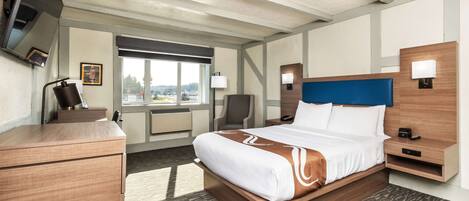 Quarto de hotel com uma cama grande, uma escrivaninha, uma cadeira, uma televisão e janela com vista para a cidade.