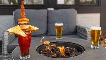 A table with a drink, a fire pit, and two glasses of beer.