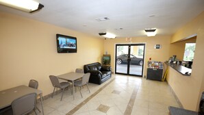 A lobby with a reception desk, a seating area with a couch and chairs, a television mounted on the wall, and a tiled floor. - Days Inn by Wyndham DeFuniak Springs (De Funiak Springs)