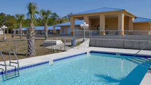 A swimming pool with a blue tiled edge, a metal ladder, and a covered area with a yellow roof. - Days Inn by Wyndham DeFuniak Springs (De Funiak Springs)