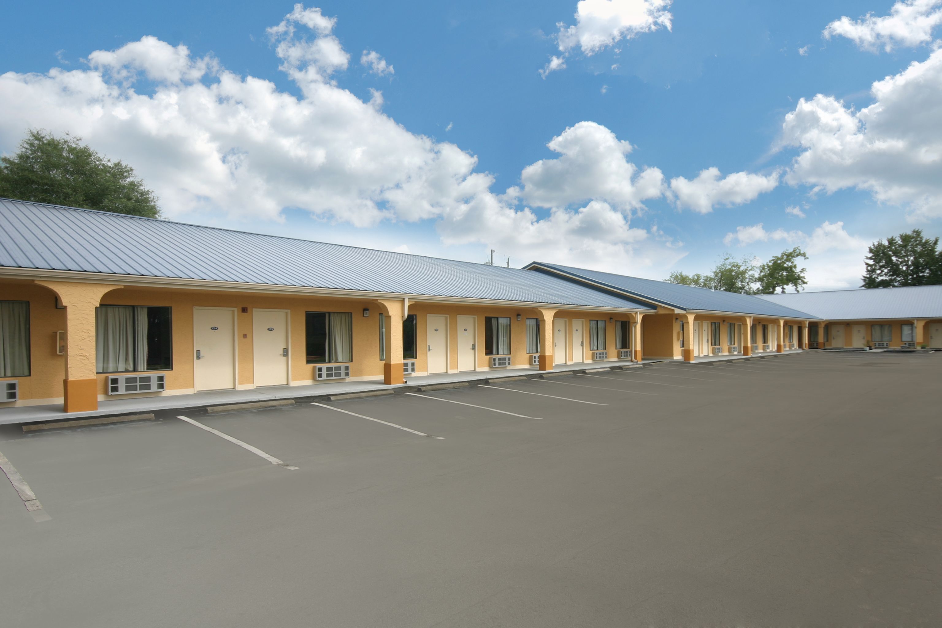 A row of motel rooms with a parking lot in front.