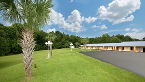 A hotel with a large parking lot, a grassy lawn, and a palm tree. - Days Inn by Wyndham DeFuniak Springs (De Funiak Springs)