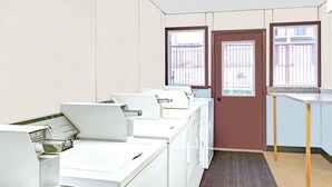 A laundry room with multiple washing machines, a door, and windows with metal bars. - Days Inn by Wyndham Washington Pennsylvania (Washington)