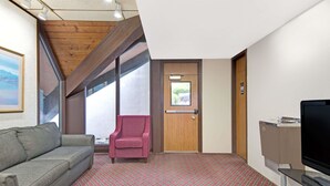A room with a wooden ceiling, a red armchair, a grey sofa, a television, and a patterned carpet. - Days Inn by Wyndham Washington Pennsylvania (Washington)