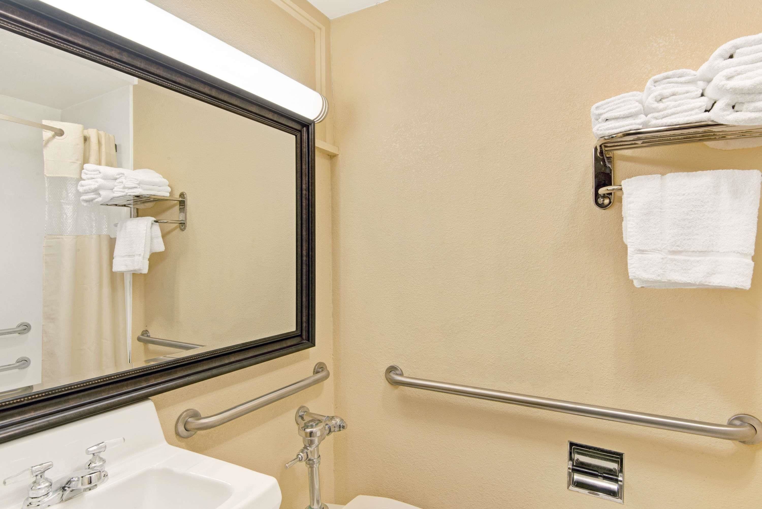 A bathroom with a sink, mirror, towel rack, and grab bars.