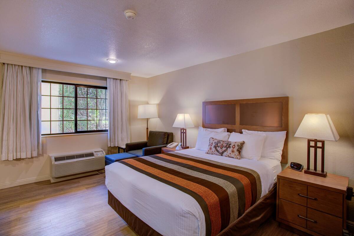 A hotel room with a large bed, two bedside tables with lamps, a chair, a desk, and a window with curtains.