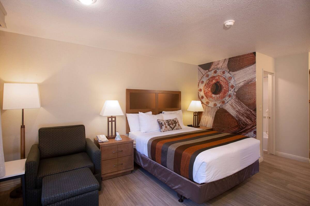 A hotel room with a bed, bedside tables, a chair, and a large wall mural.