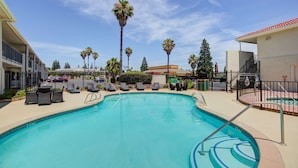 Ein Swimmingpool mit Liegestühlen, Palmen und einem Gebäude im Hintergrund.