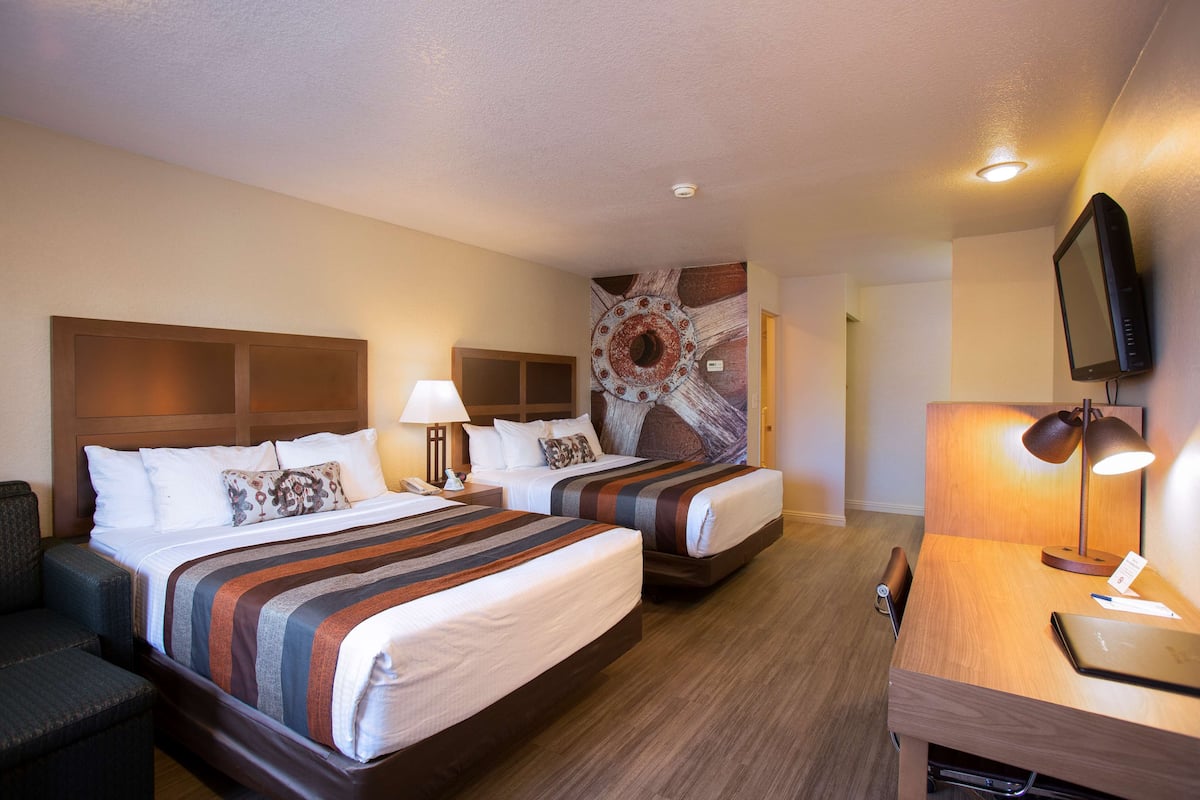 A hotel room with two beds, a desk, a chair, a TV, and a wall mural.