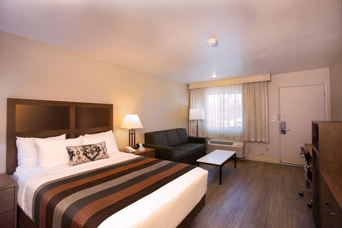 A hotel room with a large bed, a sofa, a small table, and a desk.
