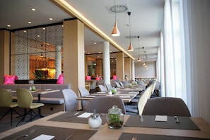 A modern restaurant with long tables, chairs, and pendant lighting.