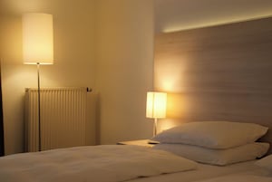 Una habitación de hotel con cama, lámpara de noche y radiador.