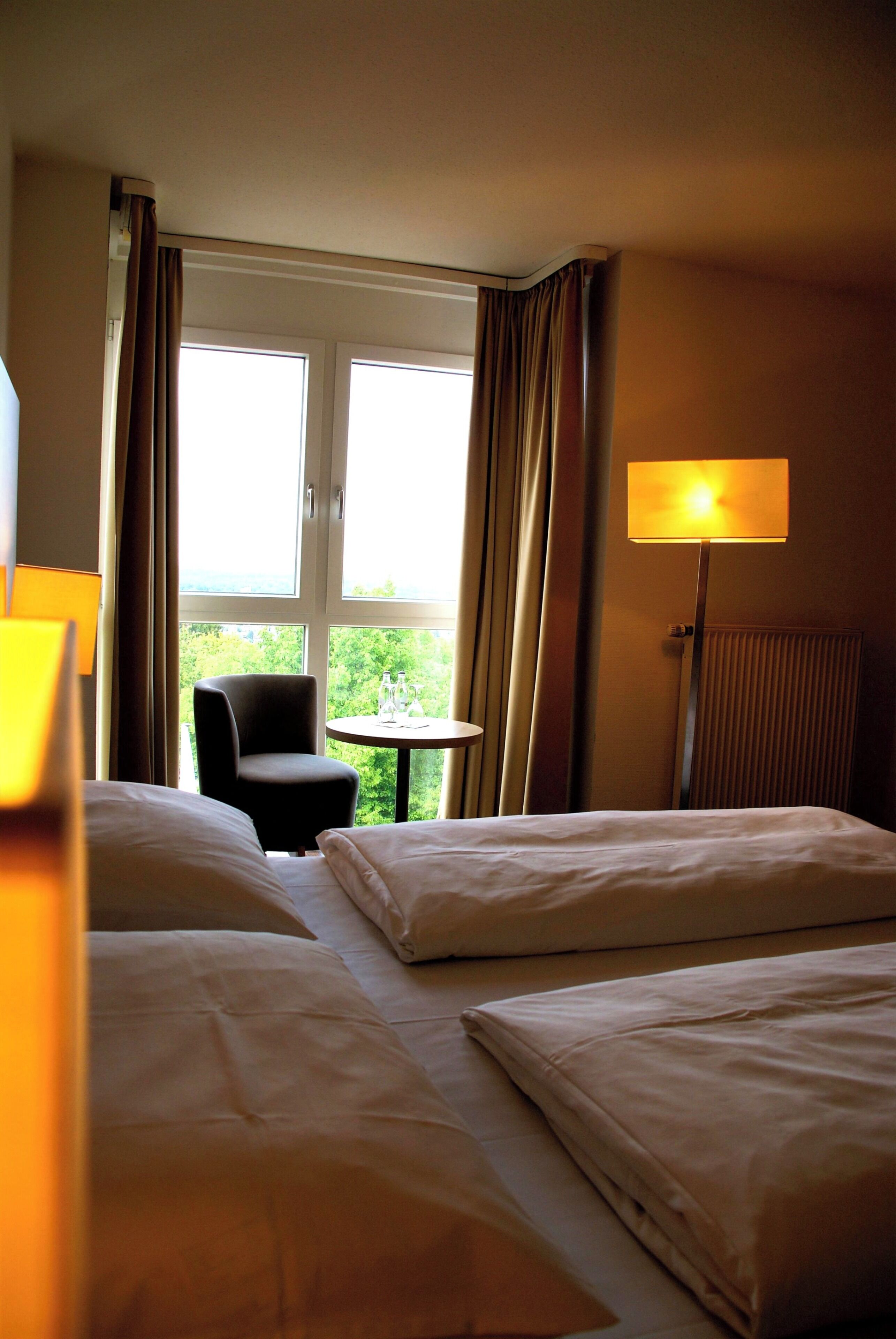 Habitación de hotel con dos camas, una silla, una mesita y una ventana con cortinas.
