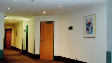 A hotel corridor with carpeted flooring, a wooden door, and a framed picture on the wall.