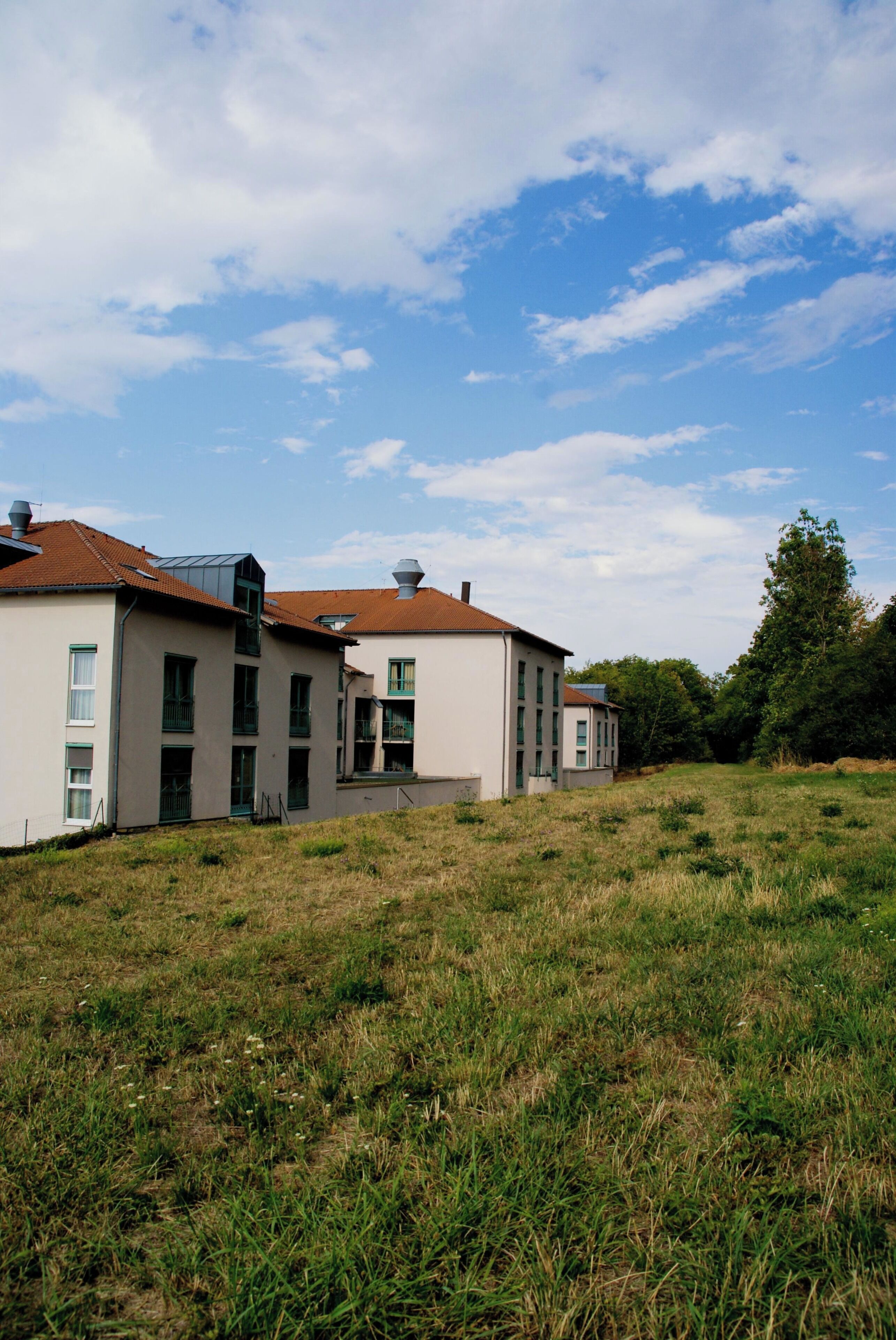 A modern building with multiple windows and a flat roof, surrounded by a grassy field.